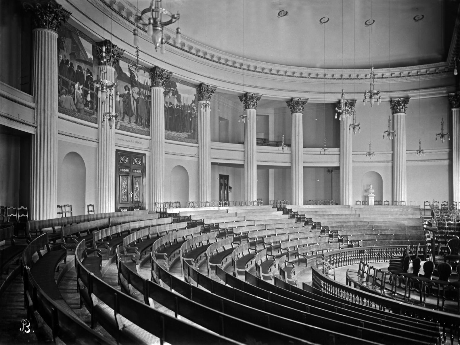The great hall of the University of Helsinki main building — curved rows of wooden benches beneath Corinthian columns — in an early black-and-white photograph by Signe Brander.