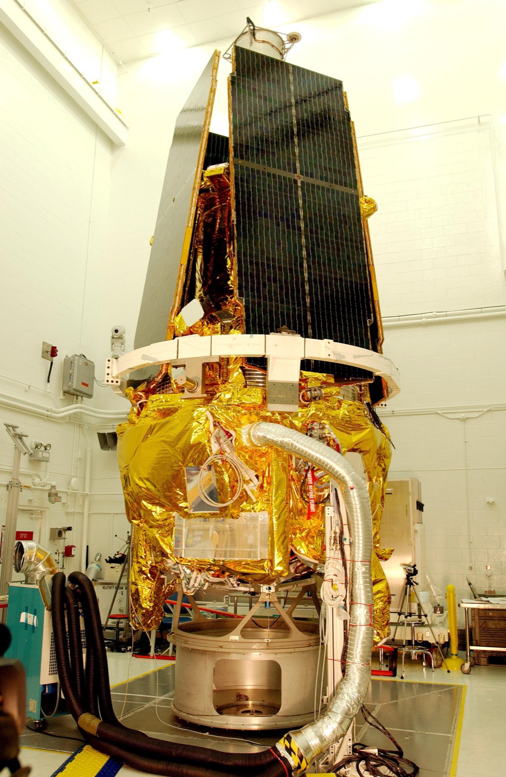 The Gravity Probe B spacecraft, wrapped in gold foil with dark solar panels folded upward, standing in NASA's payload processing facility at Vandenberg.