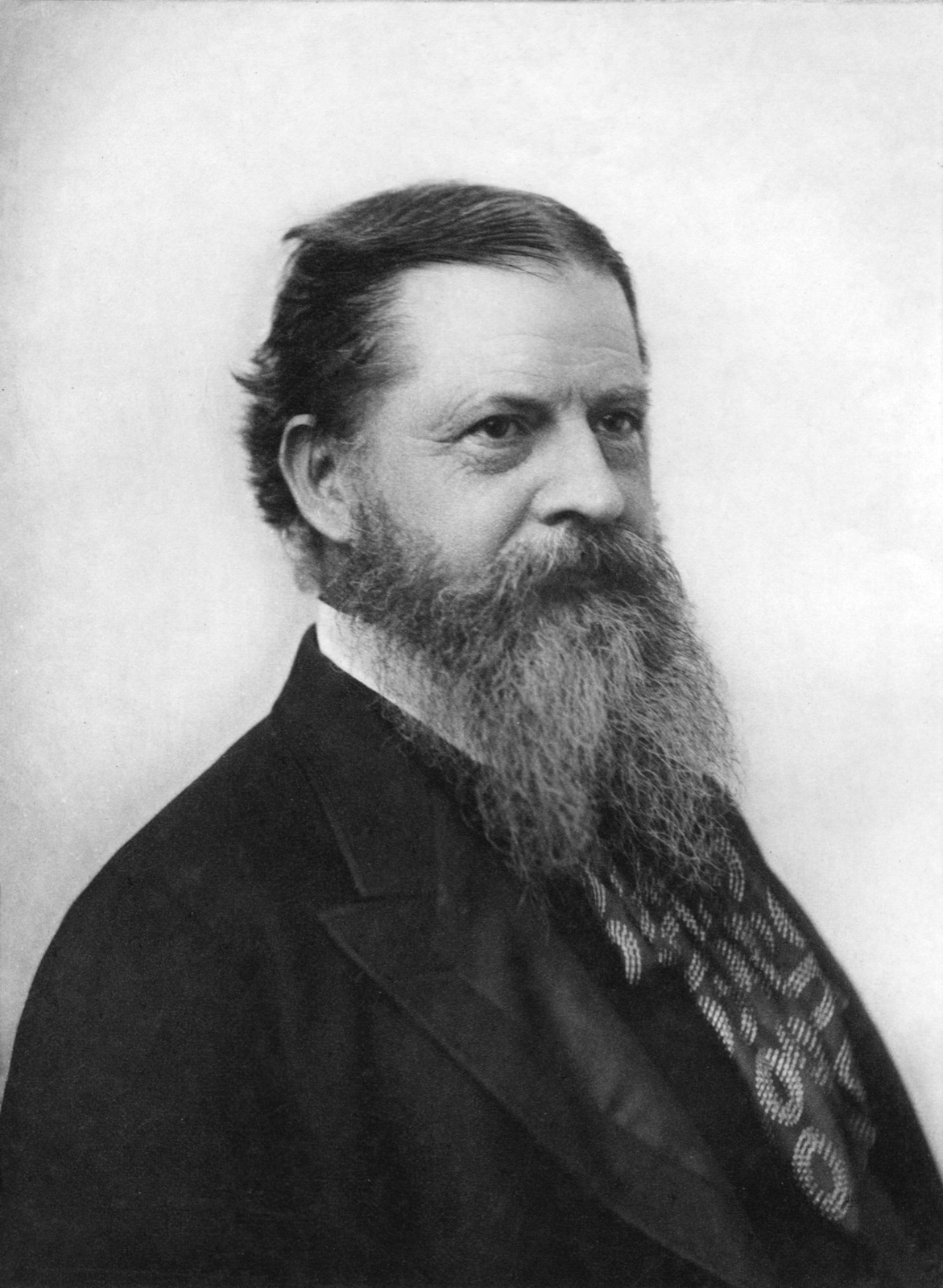 Black-and-white studio portrait photograph of Charles Sanders Peirce, bearded, in a dark coat.