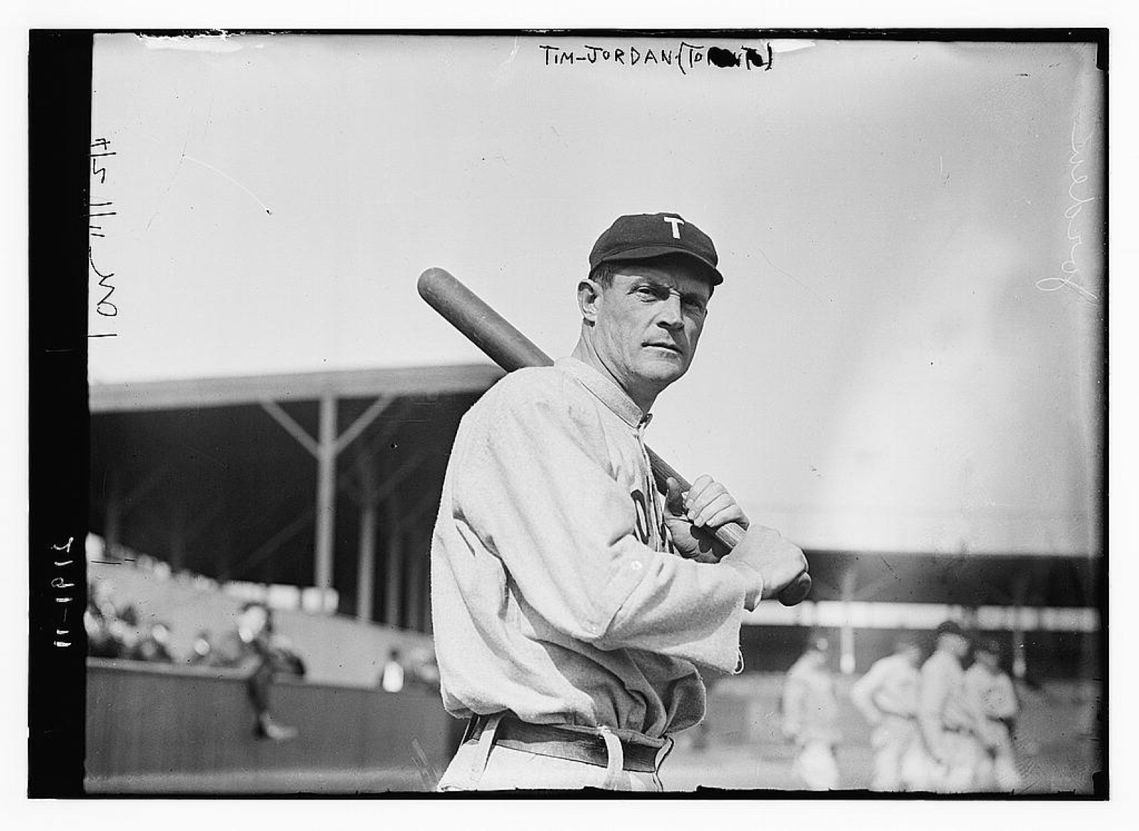 Baseball first baseman Tim Jordan of the 1911–1912 Toronto club posing with a bat on his shoulder, ballpark grandstand behind him.