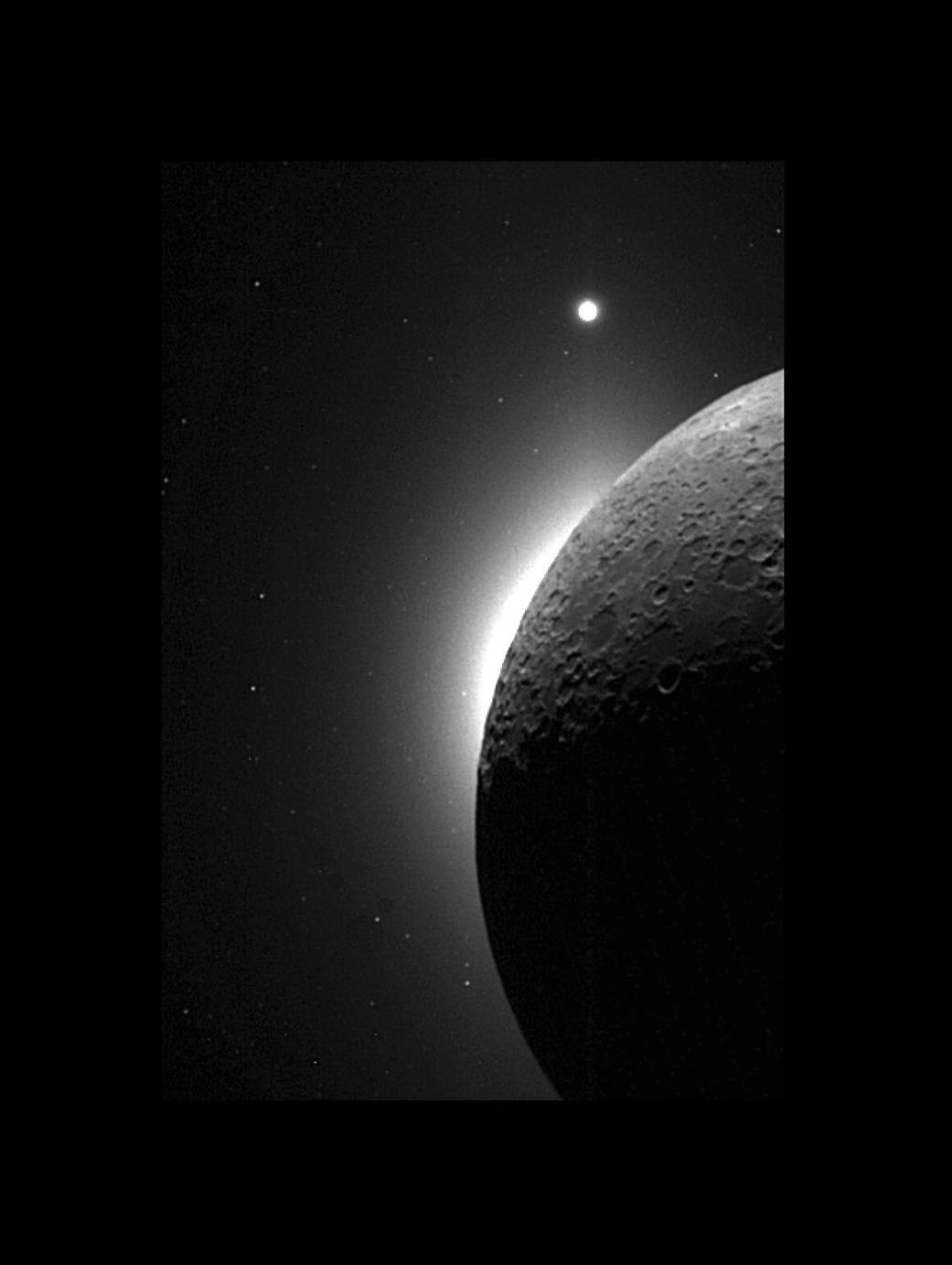 A dark space photograph from the Clementine probe: the unlit disc of the Moon in silhouette at the center, the pale feathered glow of the Sun's corona spreading from behind it, and a single bright point of light — the planet Venus — off to the side.