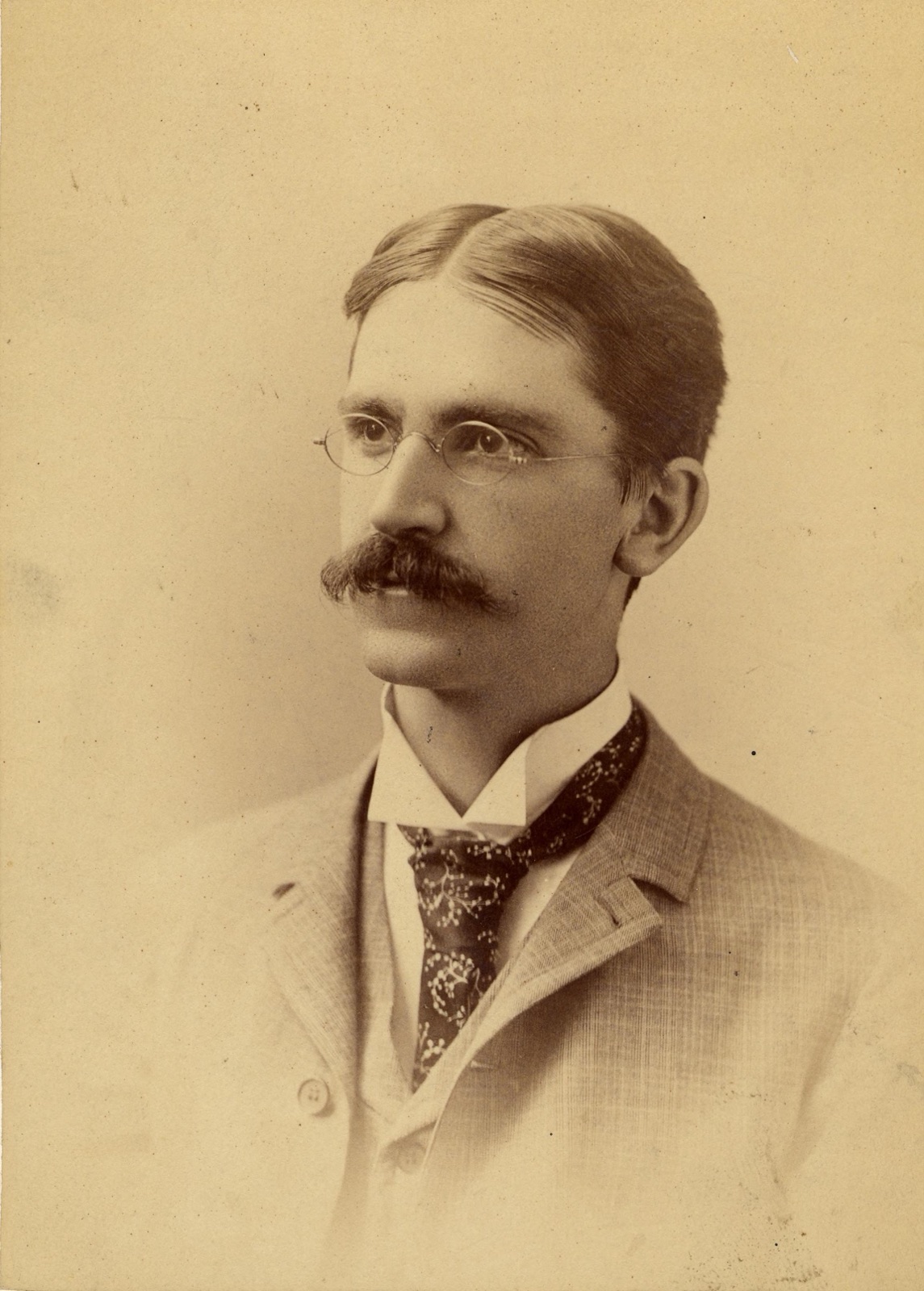 A sepia studio portrait photograph of the philosopher John Dewey as a young man, circa 1890, in a dark jacket and tie.